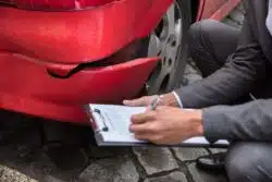 Closeup of male insurance adjuster checking damaged car bumper