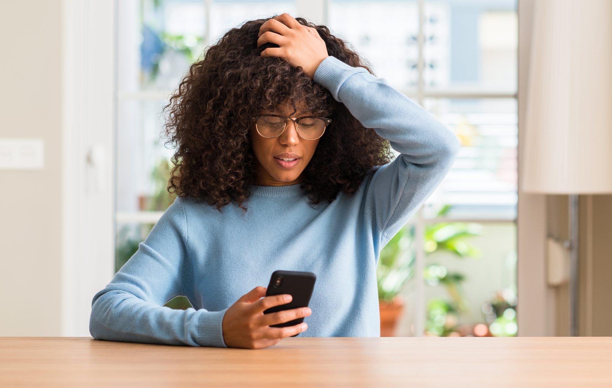 Upset woman holds hand on her head and looks at smartphone.