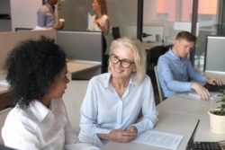 Female employees, one young and one mature, consult together at a desk