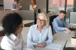 Female employees, one young and one mature, consult together at a desk
