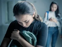 Sad young woman holds backpack to her chest as she looks down, upset
