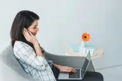 Young woman talks on phone while working on lap top