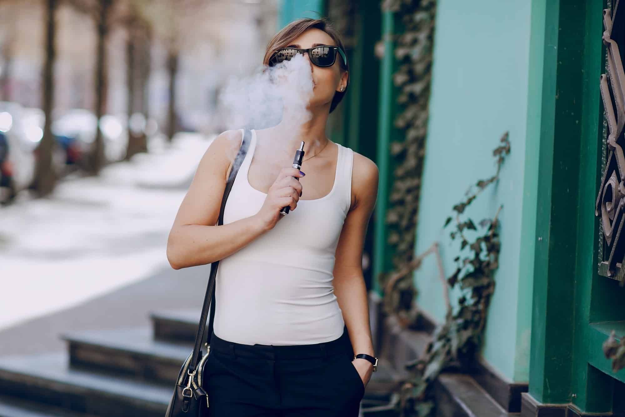 Young woman walking down street with ecigarette
