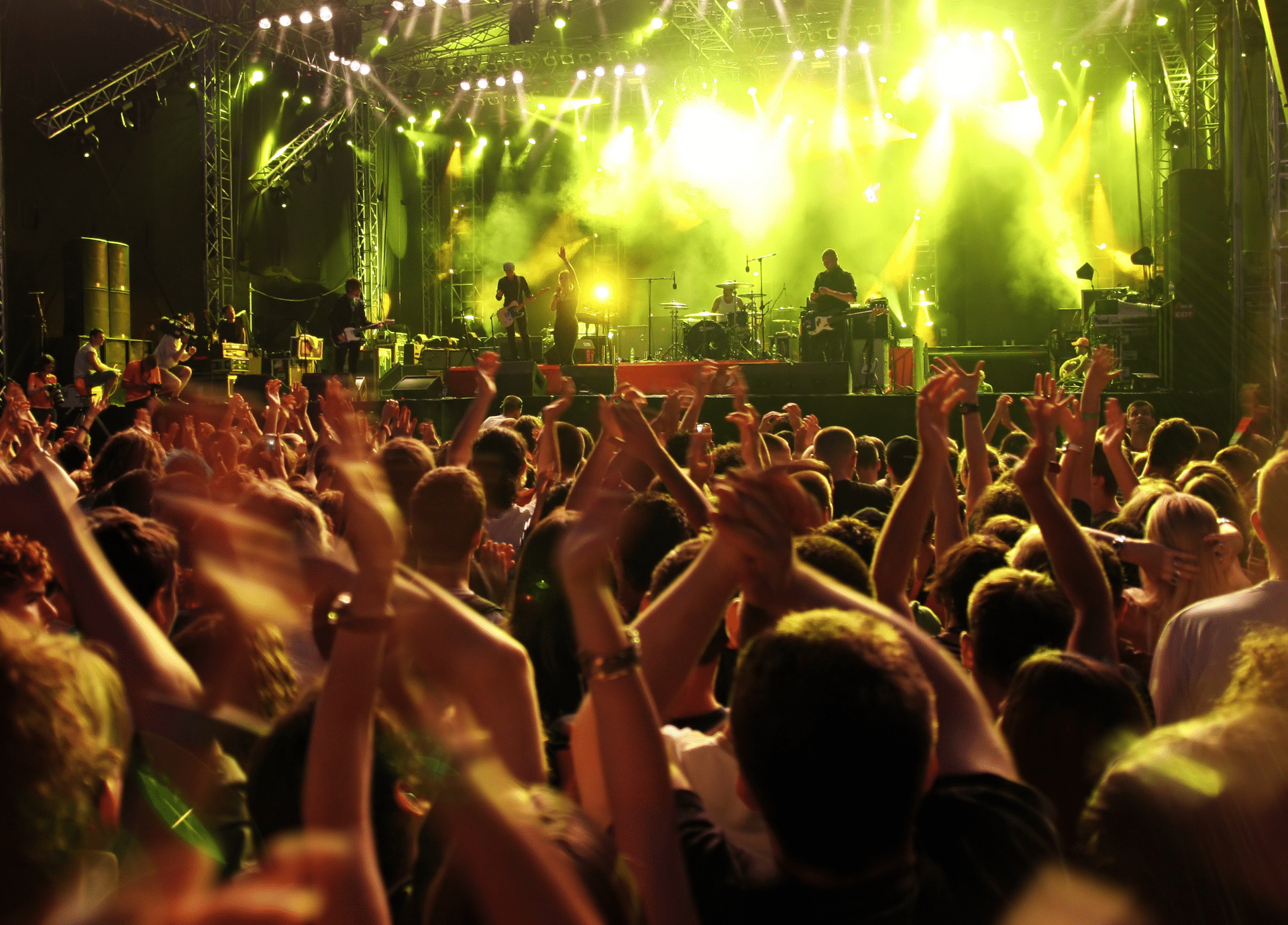 Concert crowd cheers for band on stage under yellow lights