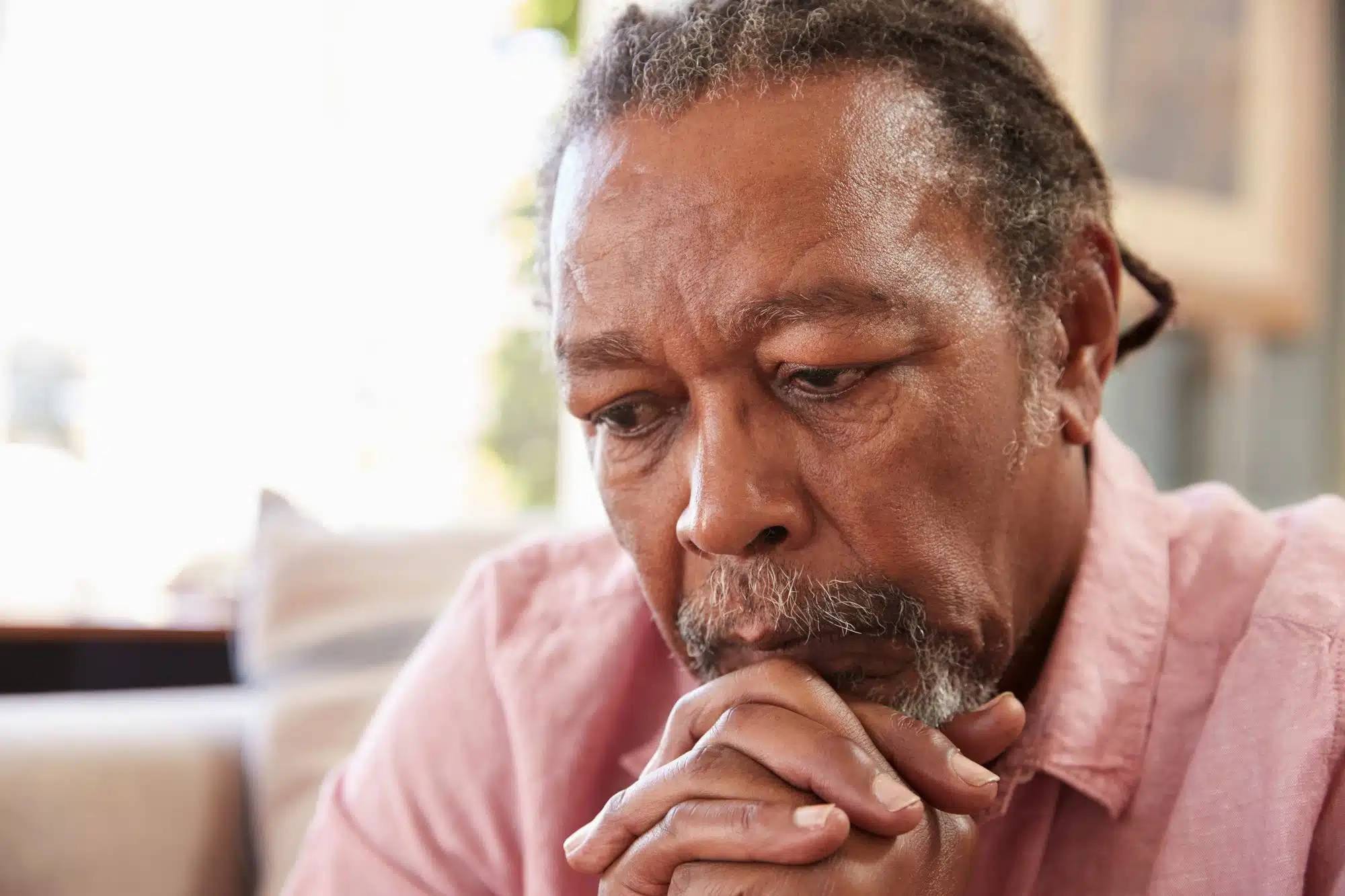 Older male contemplating with chin resting on folded hands