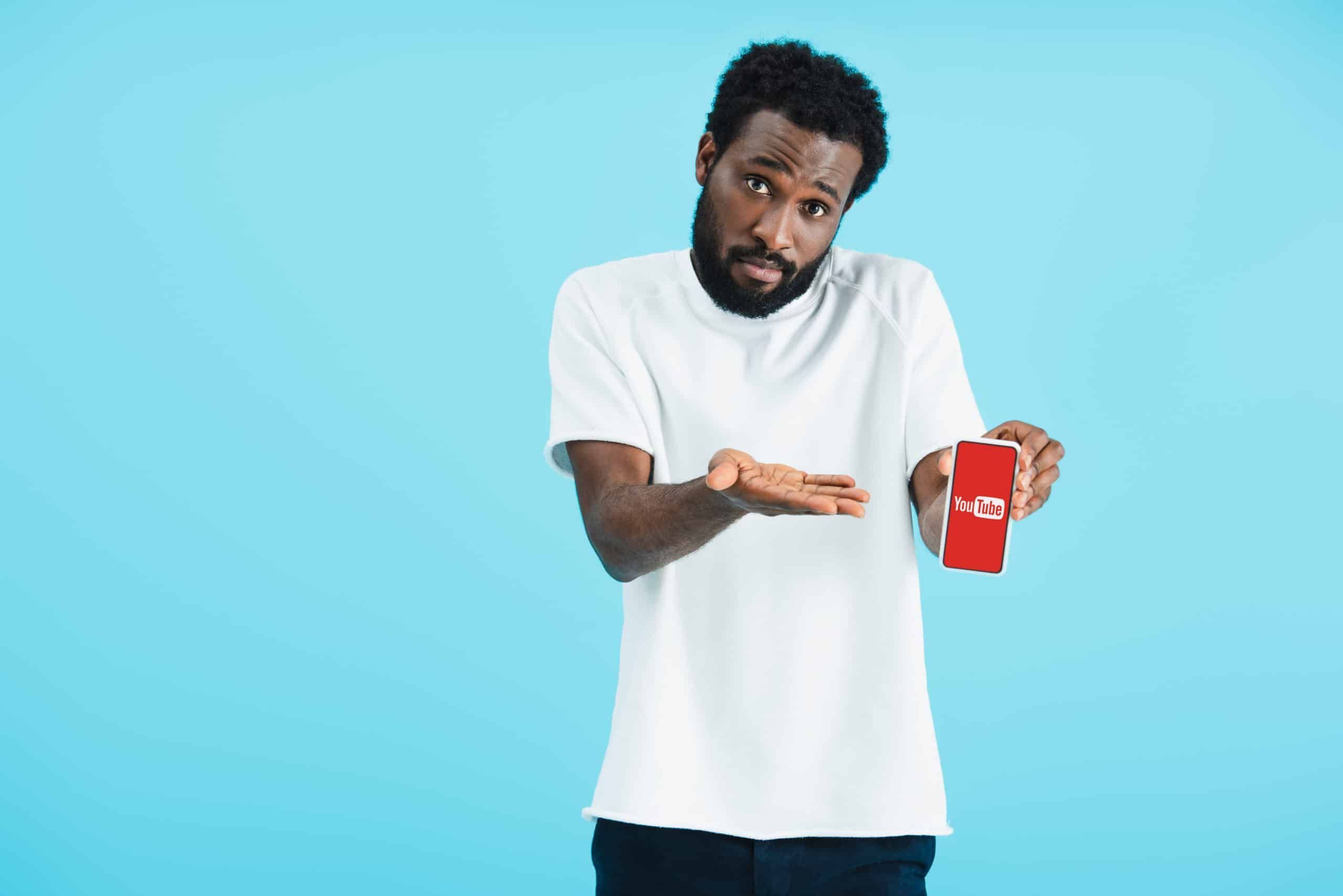 Frustrated black man in white t-shirt holds a phone displaying the YouTube logo