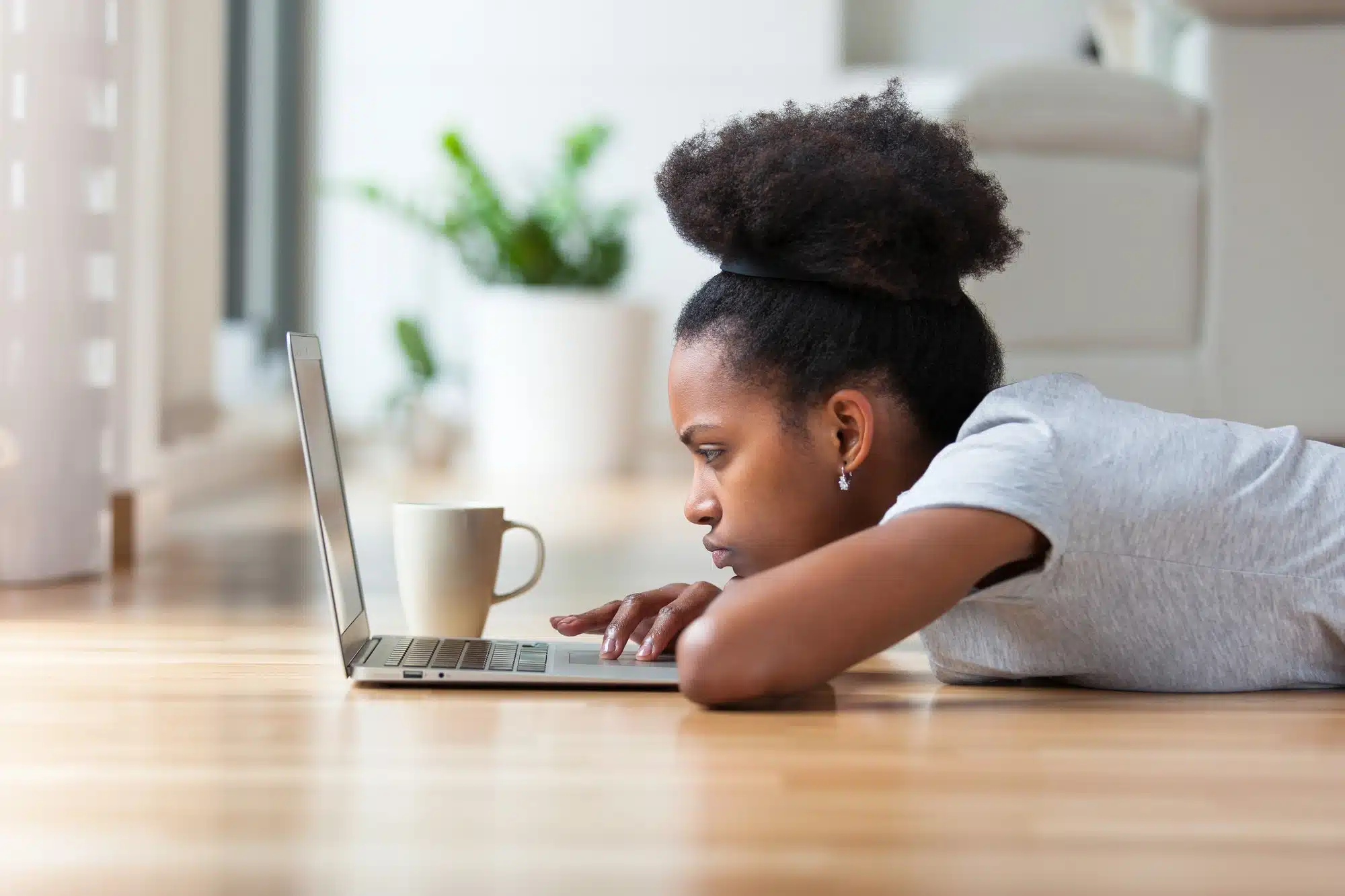 Female student lays on floor at home and works on laptop