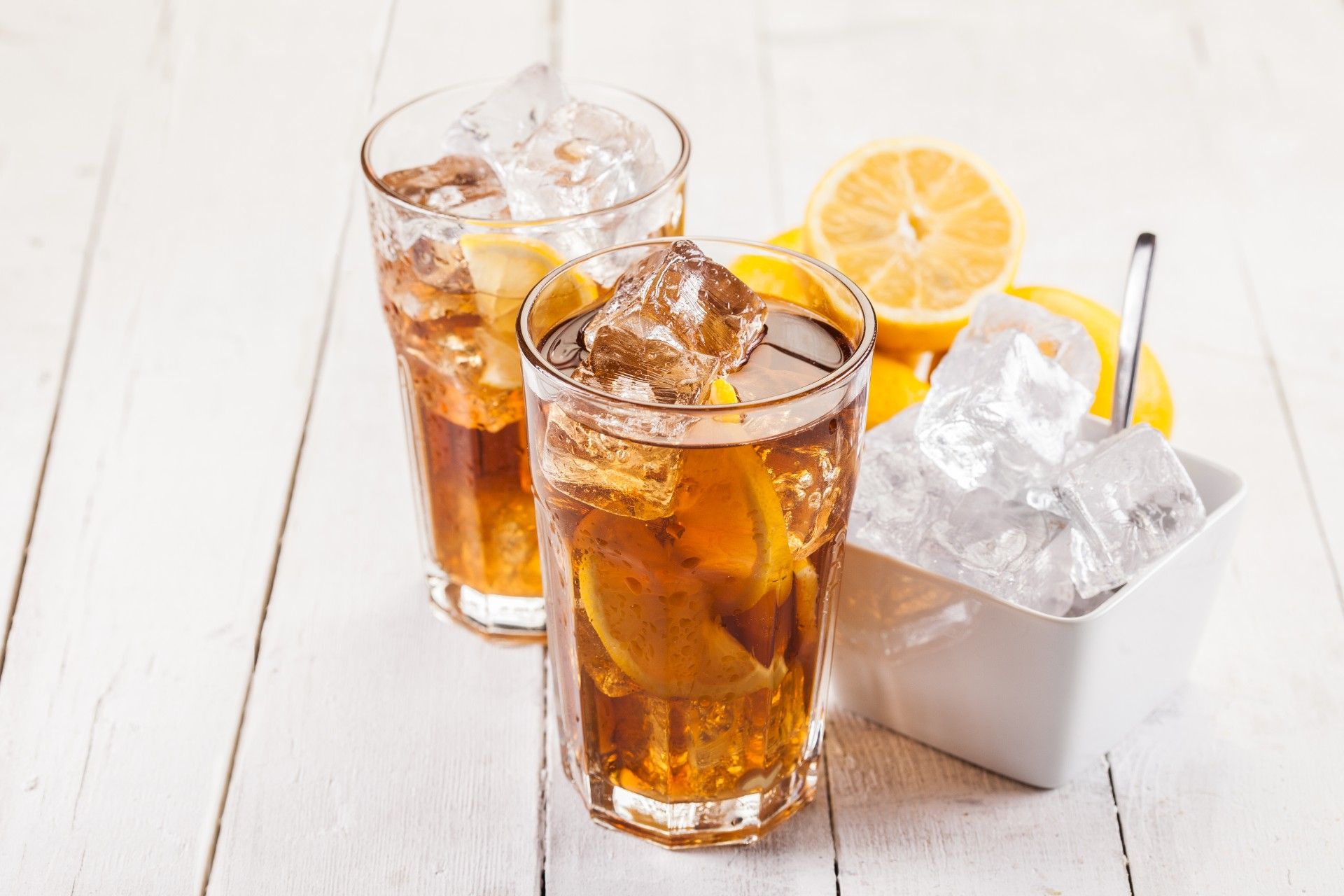 Two glasses of iced tea sitting next to bowl of ice and bowl of lemons