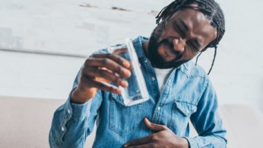 Man holds water glass in one hand and places other hand on tummy while grimacing