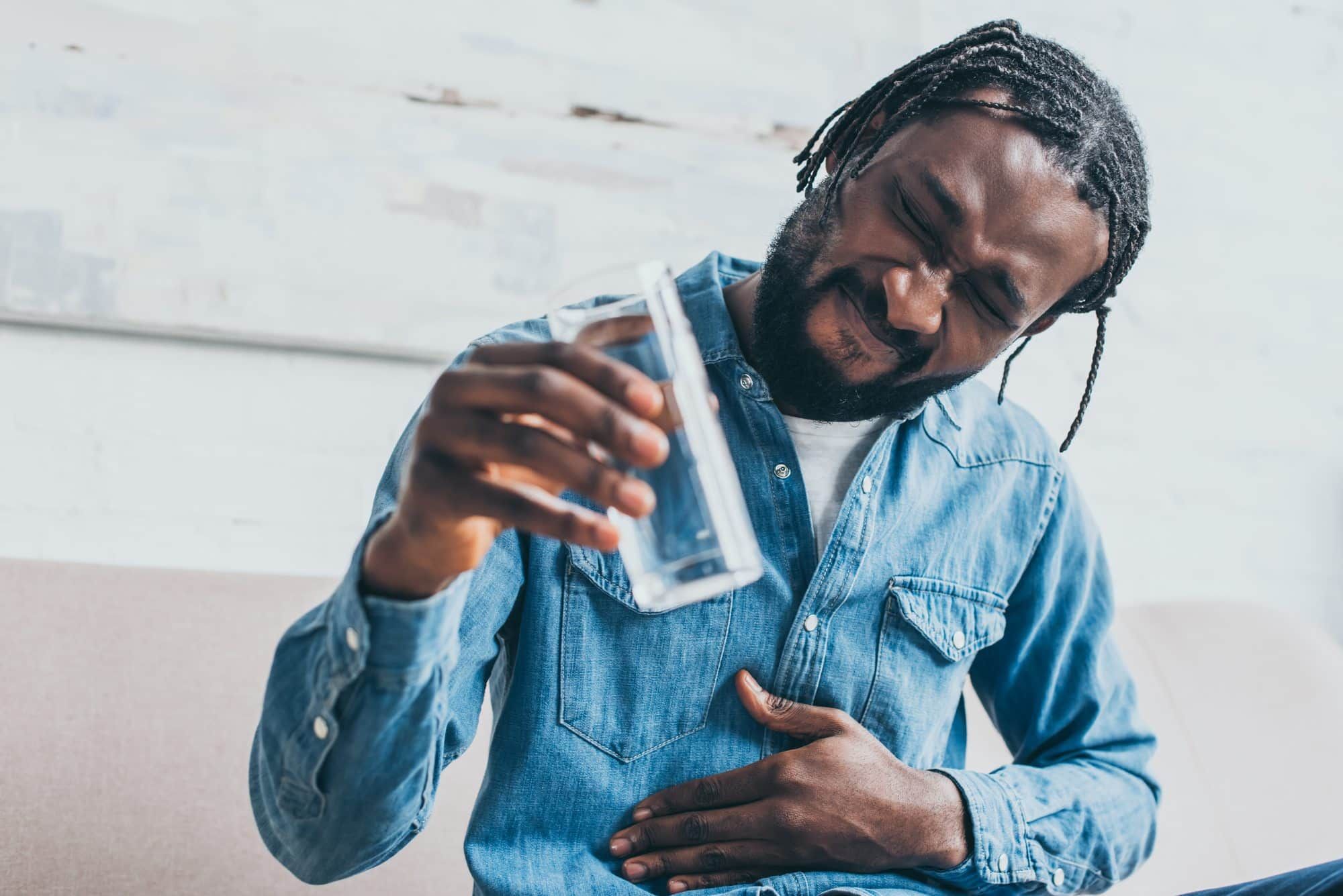 Man holds water glass in one hand and places other hand on tummy while grimacing