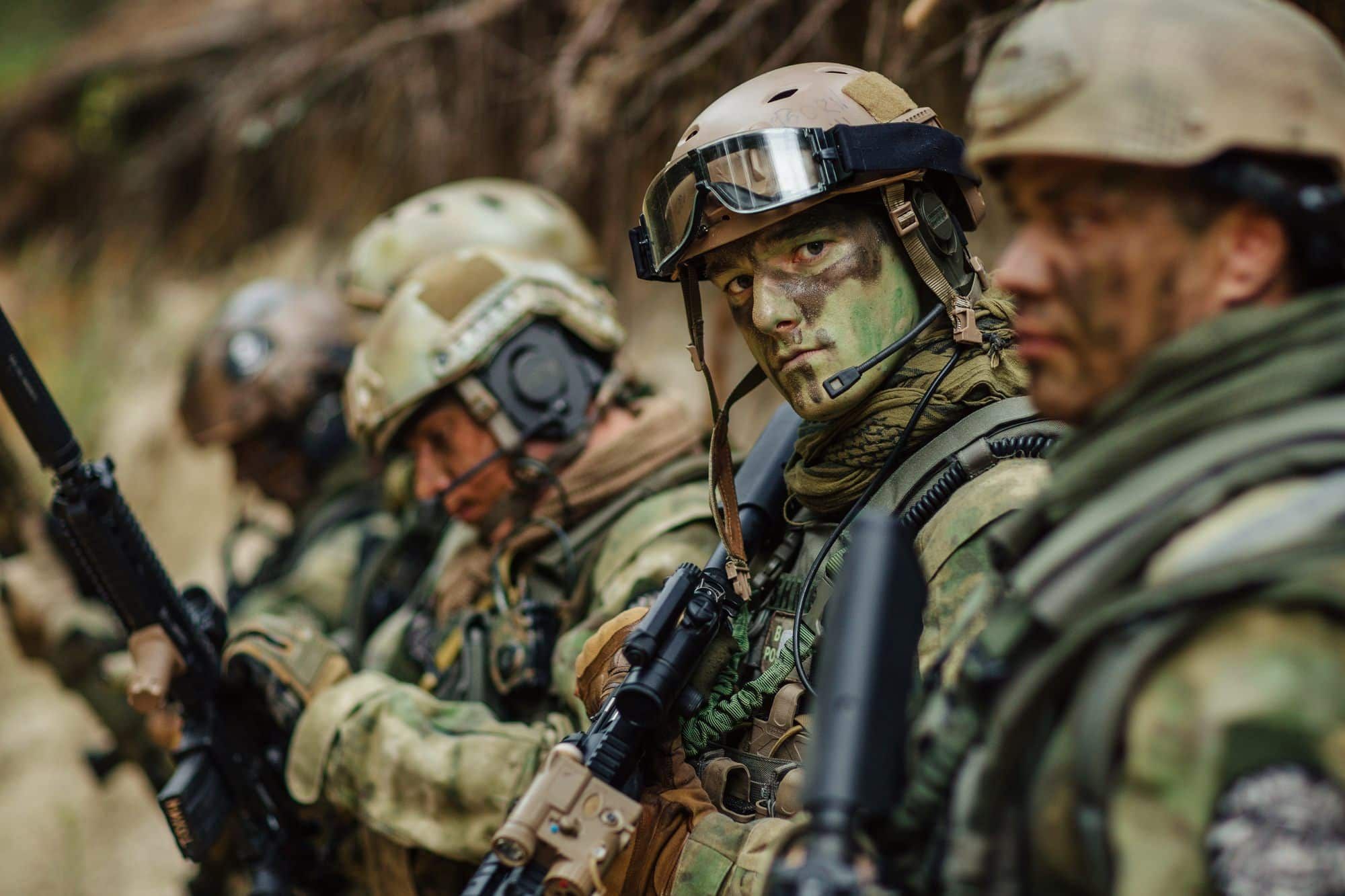 Military personnel with guns stand in line