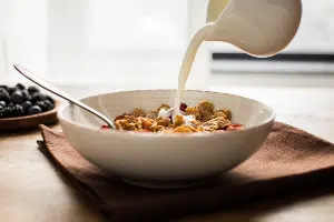 Milk being poured from pitcher over white bowl of cereal and spoon