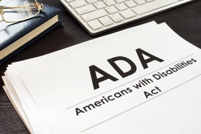 ADA paperwork on desk with computer keyboard, book and glasses