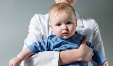 Woman in white lab coat holding a baby in a blue onesie who she recently gave Walmart pain reliever.