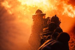 Two firefighters spray water towards a blazing fire
