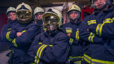 Group of firefighters in protective gear stand in front of firetruck