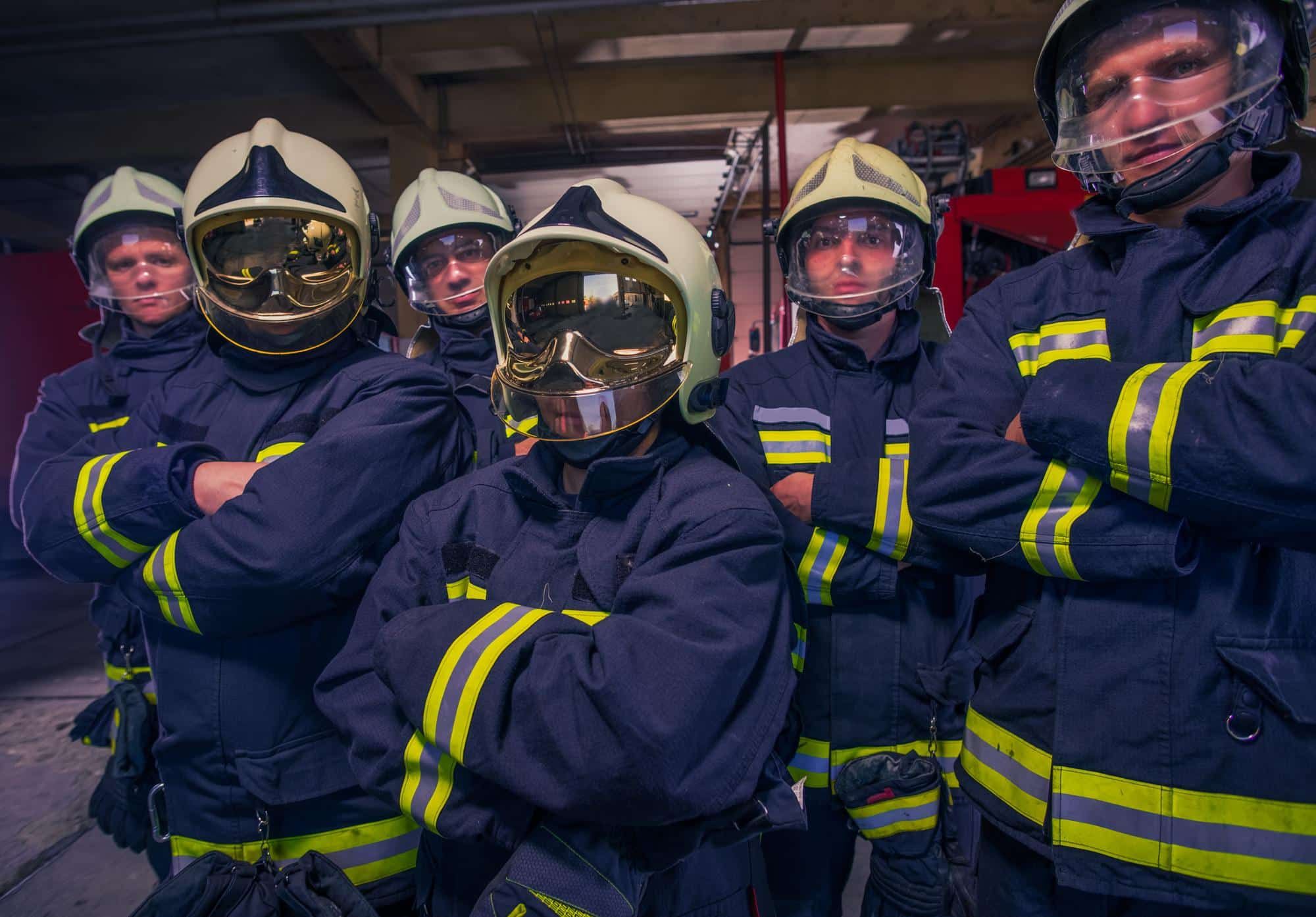 Group of firefighters in protective gear stand in front of firetruck
