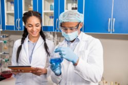 Female and male scientists look at blue liquid in lab beaker