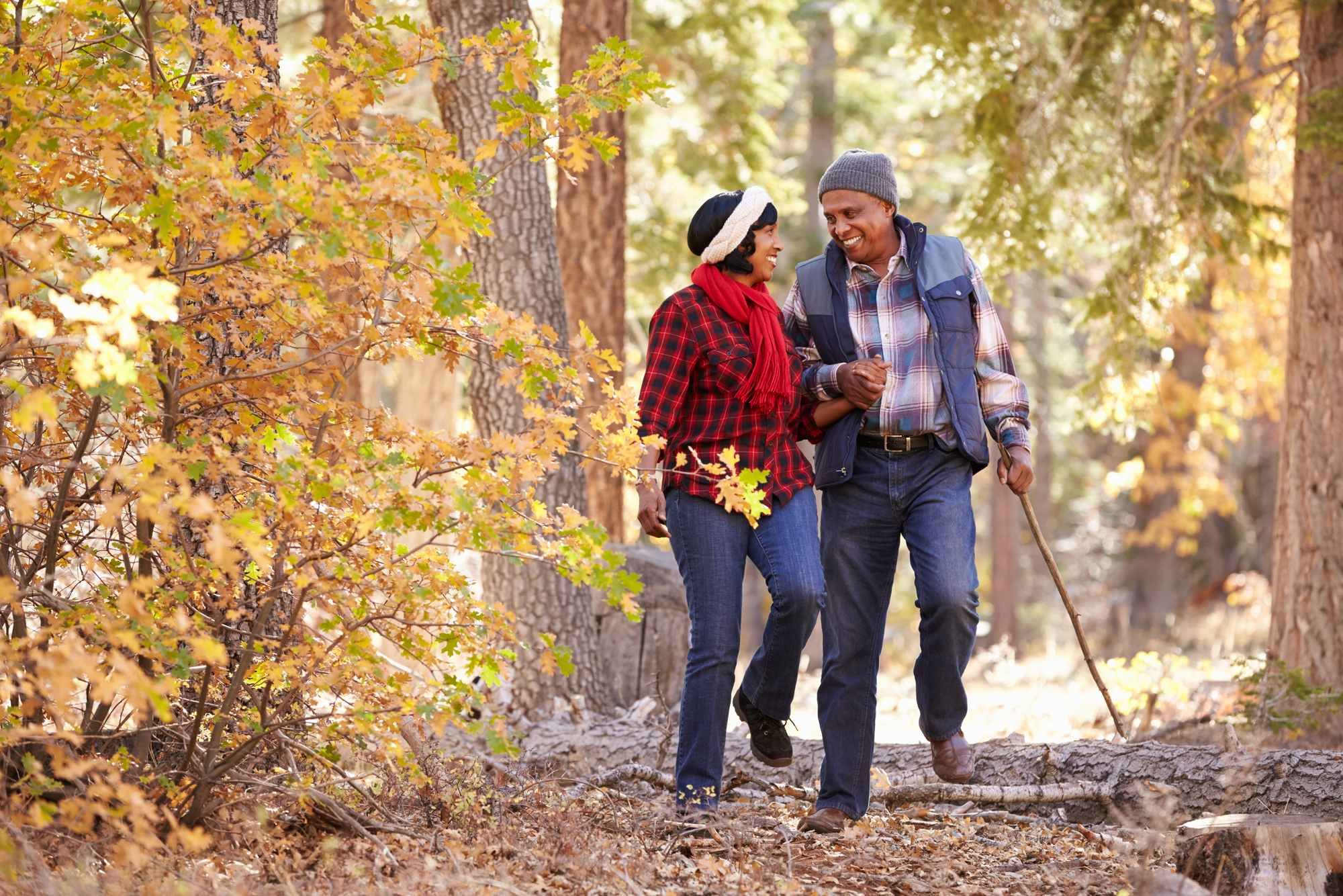 Middle aged couple walks in woods, and he uses a cane