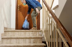 Man in protective mask and gloves leaves shopping bag of food at door of resident