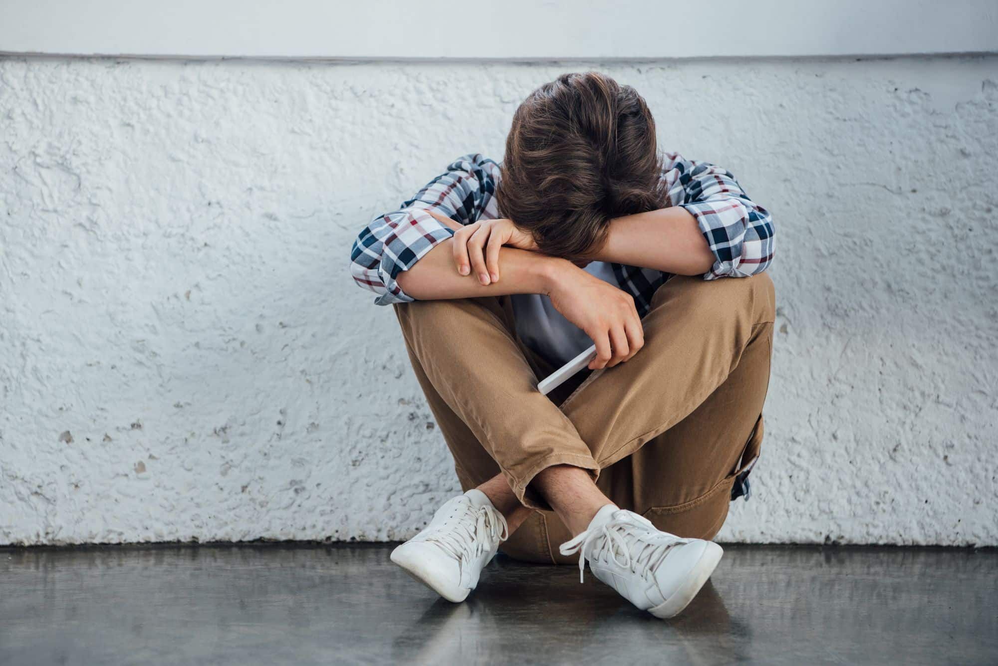 Sad teen boy sits on ground with head down