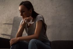 Crying woman sits on couch and holds a napkin