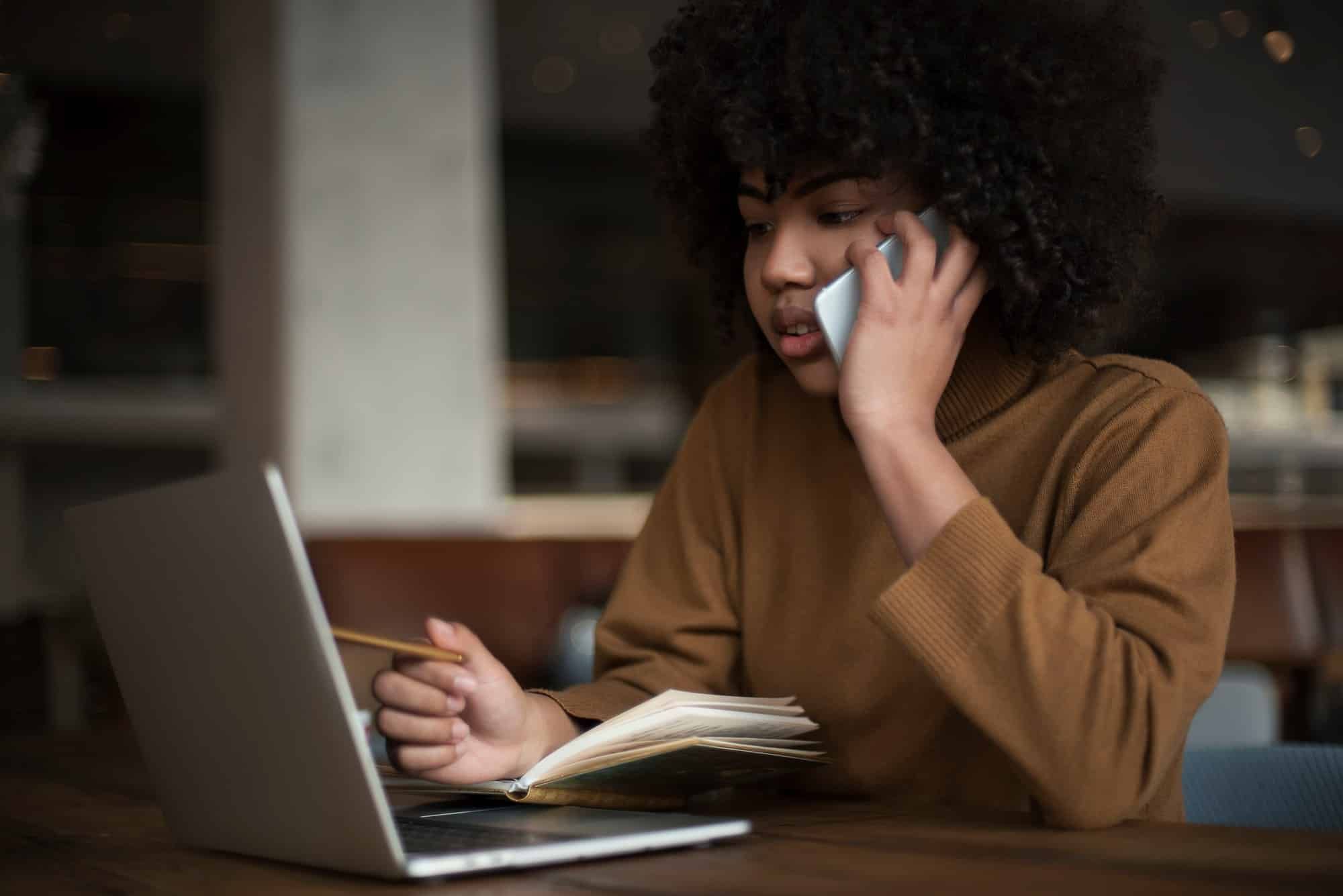 Young woman works on laptop while talking on cell phone