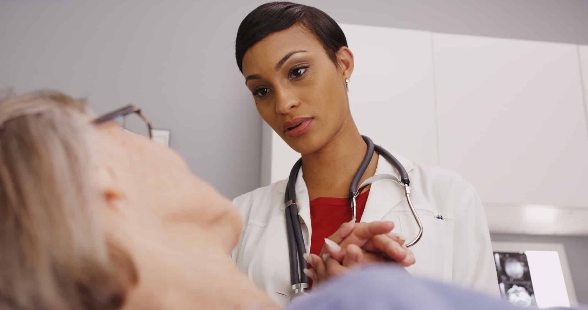 Young female doctor holds older female patient's hand in hospital