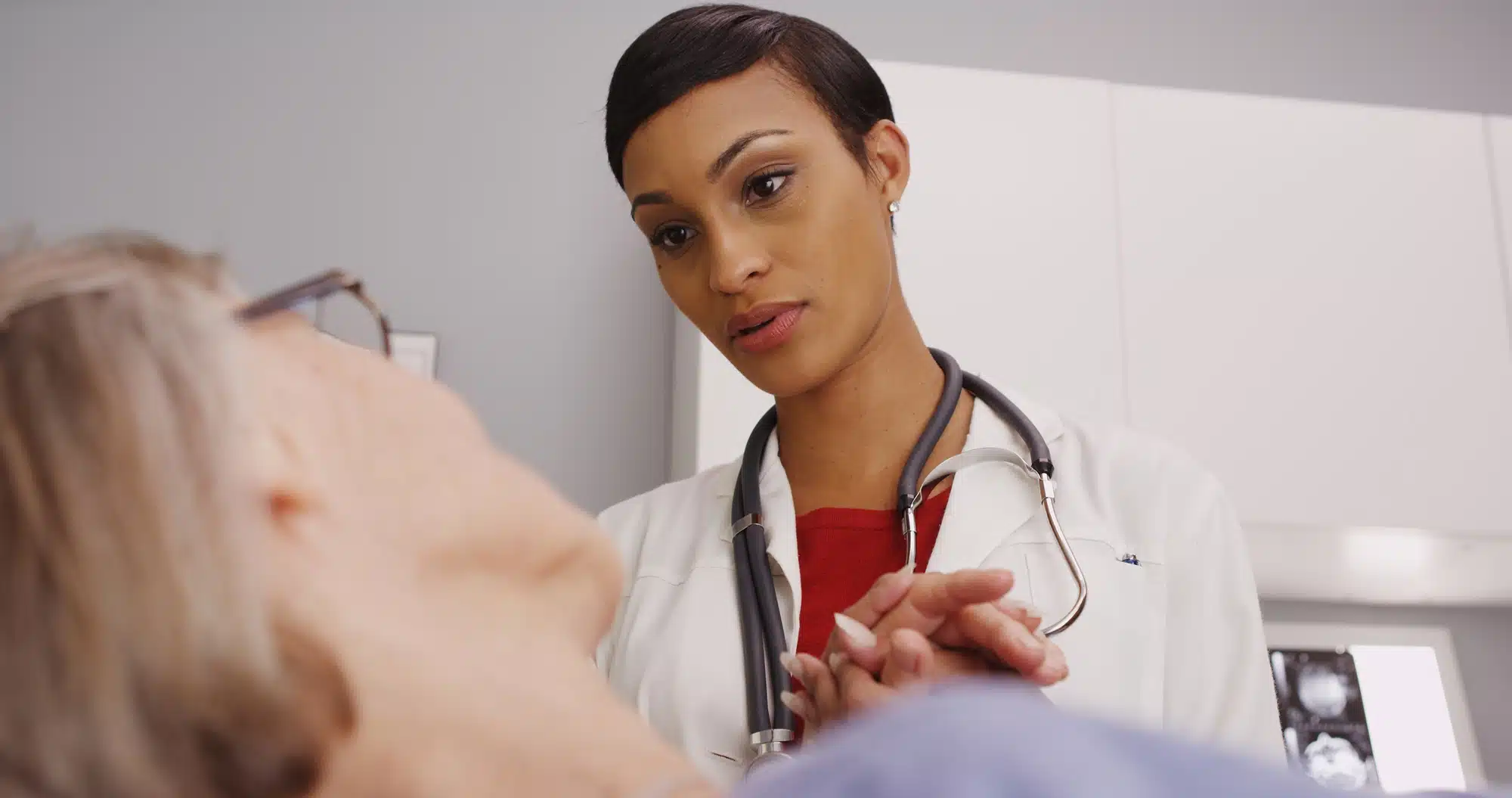Young female doctor holds older female patient's hand in hospital