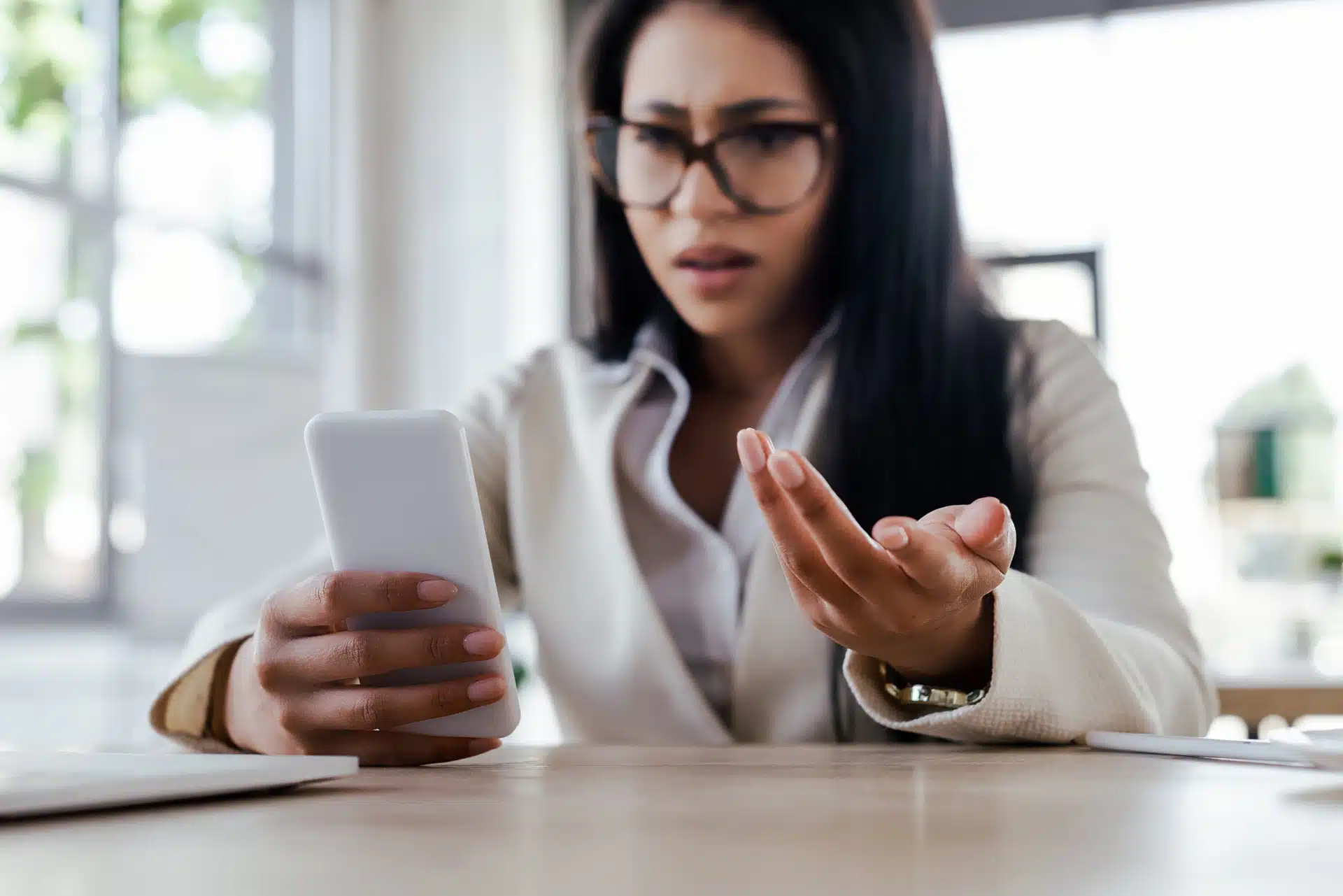Irritated dark-haired woman wearing glasses and holding smartphone