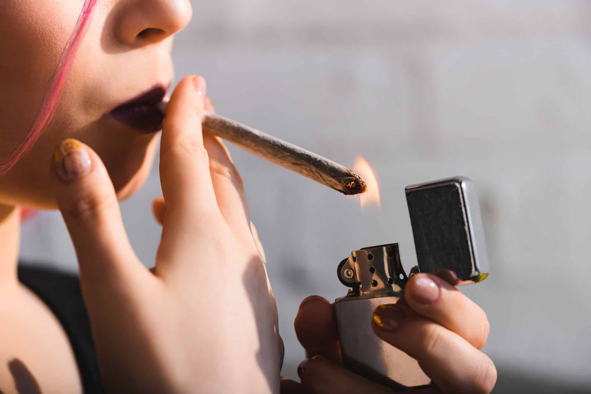 Close up of young woman lighting marijuana blunt