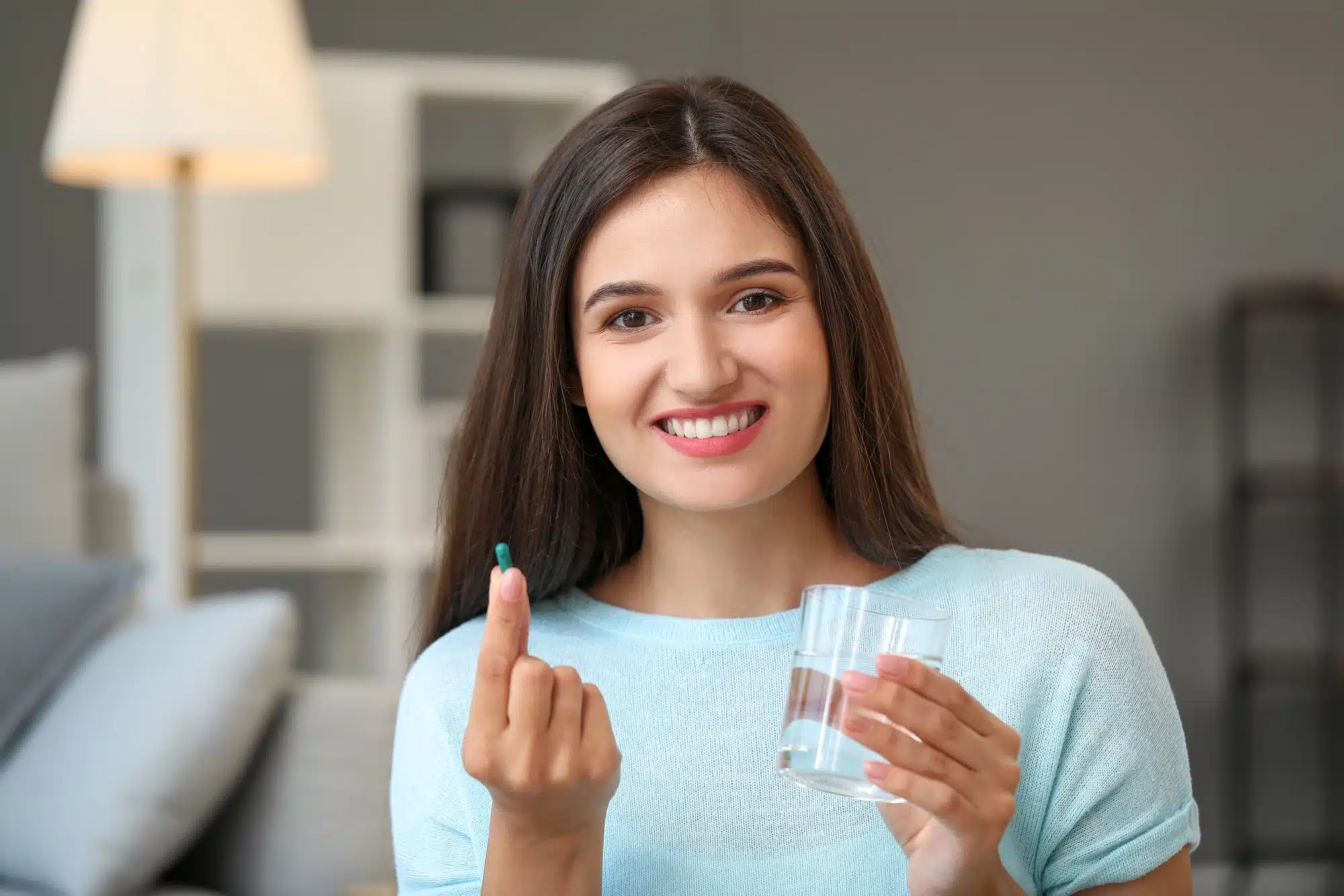 Young woman with glass of water taking a pill