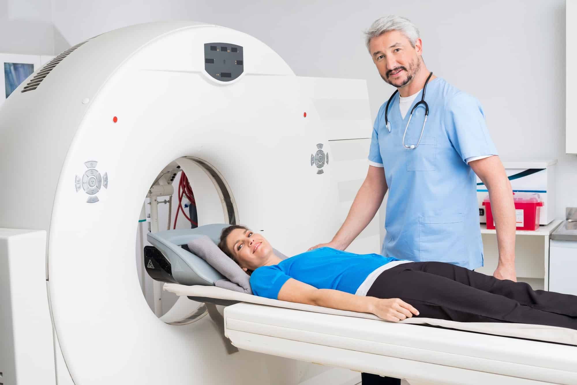 Male doctor stands next to female patient who is on MRI machine