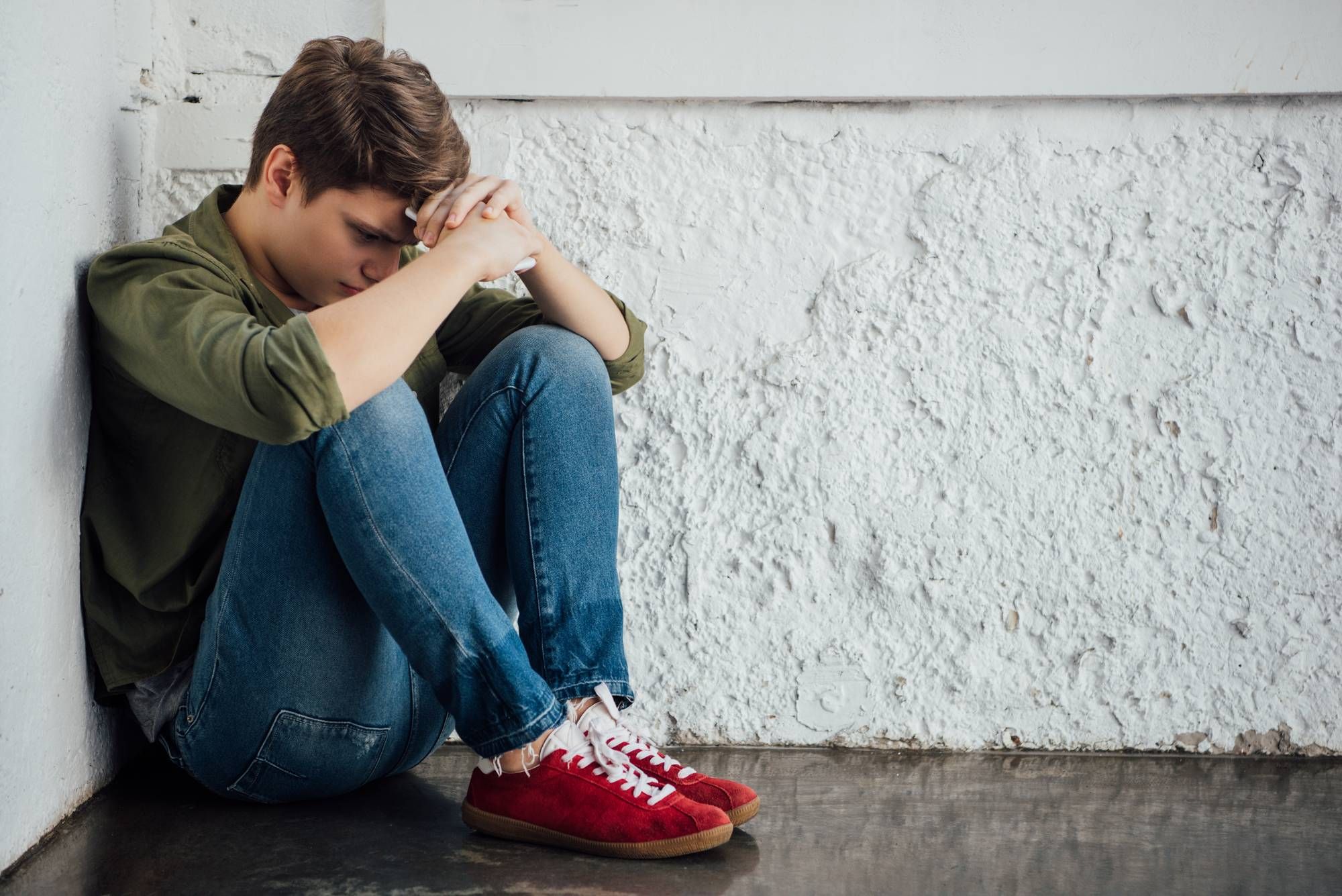 Sad teen boy sits against wall