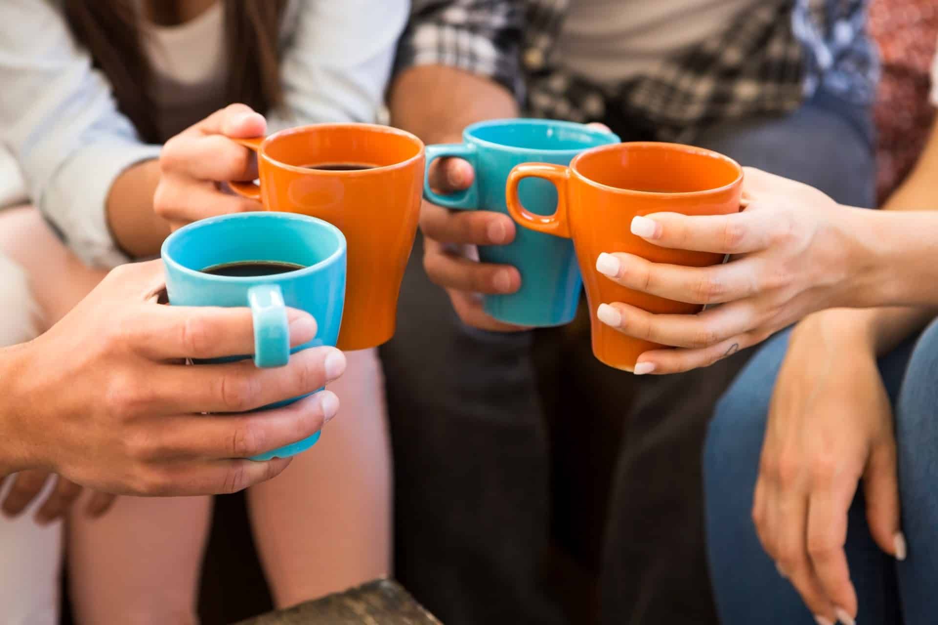 Four people hold orange and blue mugs of coffee close together - Maxwell House