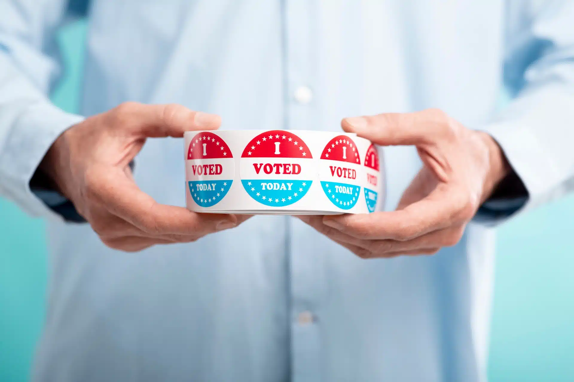 Man in blue button-down shirt holds a roll of red-white-and-blue "I voted today" stickers - Pennsylvania voters