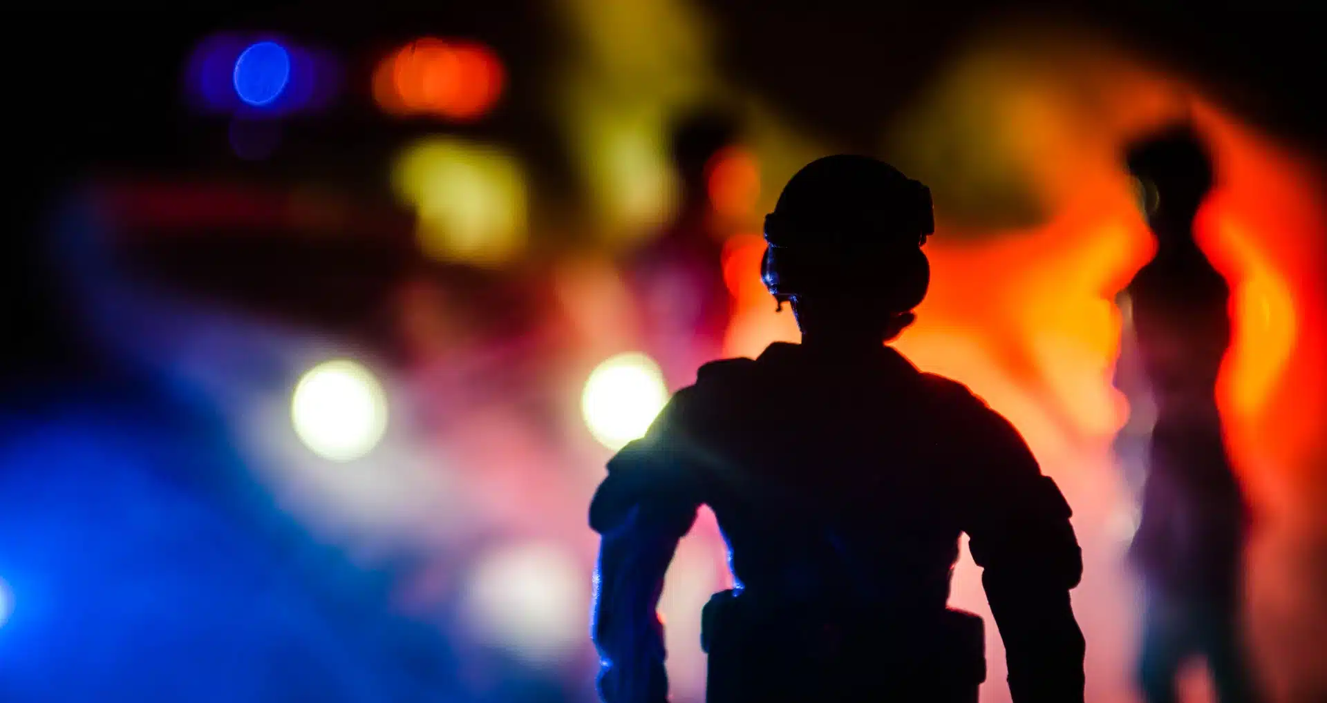 Silhouette of officer in riot gear with police lights shining at night - portland protests
