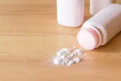 Bottle of powder on its side with some spilled onto wood table
