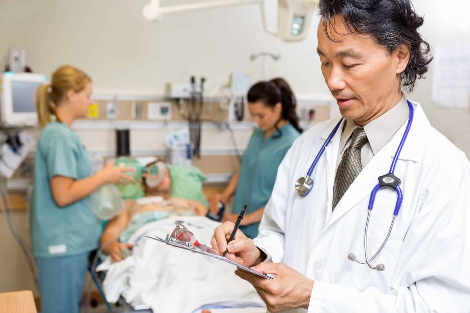 Doctor writes notes while nurses tend to patient in the background