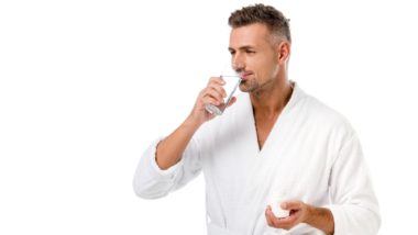 Man in white bath robe takes pills with glass of water