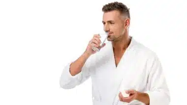 Man in white bath robe takes pills with glass of water