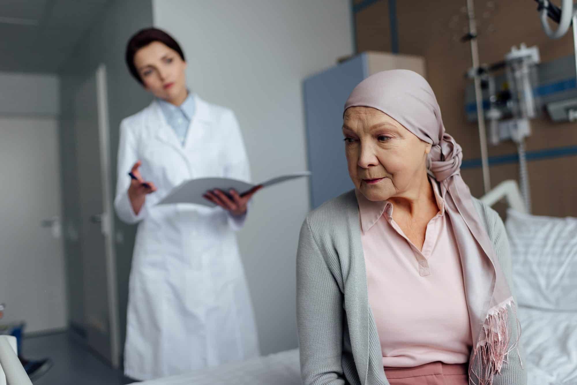 Elderly woman with cancer sits on edge of hospital bed
