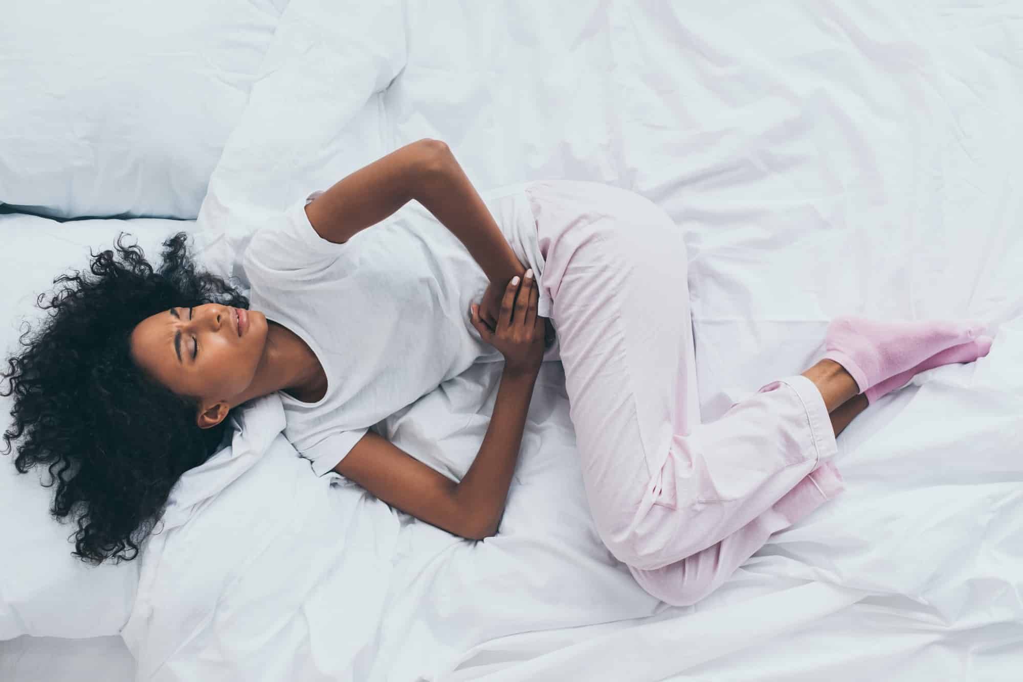 Woman suffering abdominal pain lies on bed