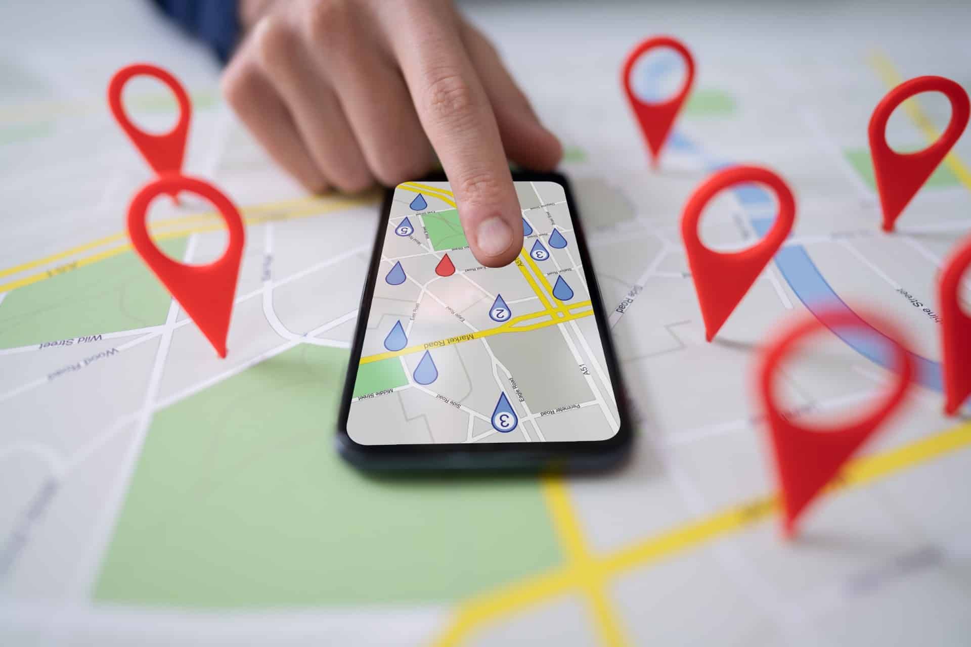 A person uses a map on a smartphone lying on top of a map showing red location markers - Google location tracking