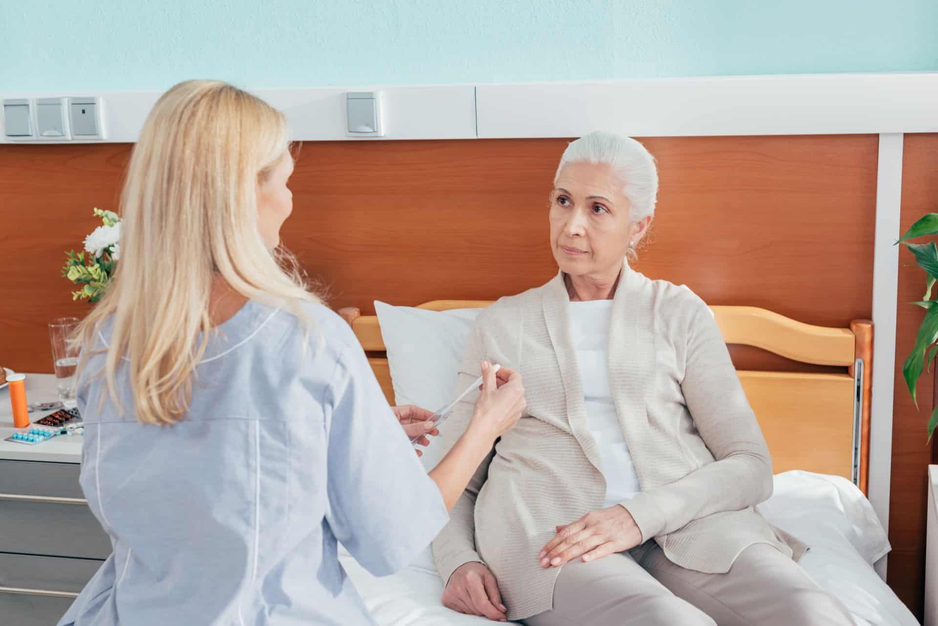 A female nursing home employee takes a female patient's temperature as the patient sits in bed - nursing homes