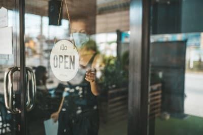 A woman in a mask turns the "open" sign around on a glass restaurant door - social distancing guidelines