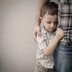 upset young male child hugging adult leg