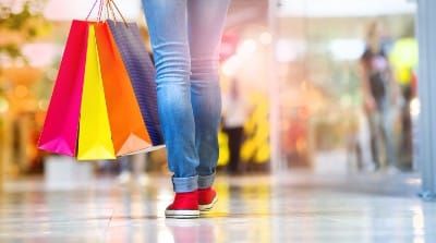 Closeup of a shopper carrying their bags low by their legs in an indoor mall