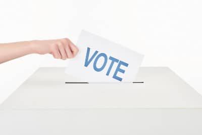 Woman's hand puts card reading "vote" in blue into white ballot box - voting rights