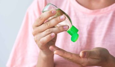A woman dispenses hand sanitizer into her hand from a bottle with a green cap